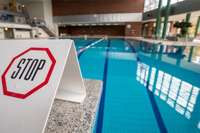 Symbolbild: „Stop“ steht auf einem Schild auf einem gesperrten Startblock am Beckenrand eines Hallenbads.