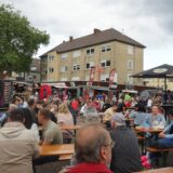 Viele Menschen sitzen auf Bänken, dahinter stehen Foodtrucks.