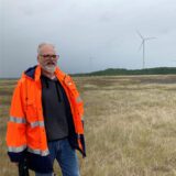 RAG-Geologe Oliver Kunz steht auf einer Halde vor einem Windrad.