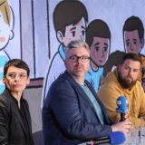 NRW-Familienministerin Josefine Paul und zwei Männer stzen auf einem Podium und schauen einen Film an. Im Hintergrund zu sehen sind Zeichnungen von unglücklichen Kindern.