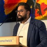 Das Bild zeigt zwei Männer in unterschiedlichen Situationen. Der Mann links steht vor einer grünen Hecke, während der Mann rechts an einem Rednerpult steht.