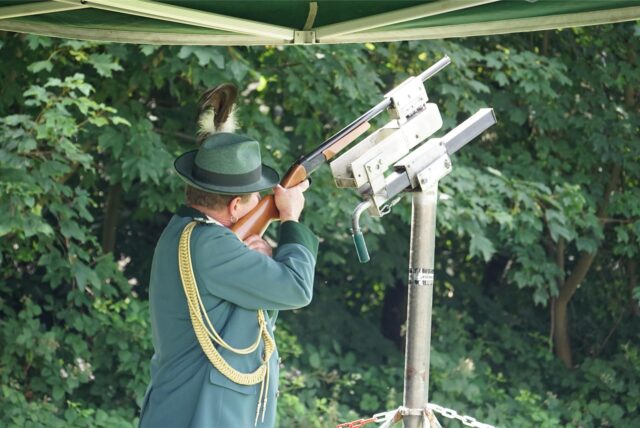 Ein Schütze des BSG Datteln Hagem in Tracht hält ein Gewehr in den Händen und zielt damit auf eine Vorrichtung. Er trägt einen grünen Hut mit Feder und eine grüne Uniform mit goldenen Verzierungen.