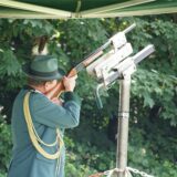 Ein Schütze des BSG Datteln Hagem in Tracht hält ein Gewehr in den Händen und zielt damit auf eine Vorrichtung. Er trägt einen grünen Hut mit Feder und eine grüne Uniform mit goldenen Verzierungen.