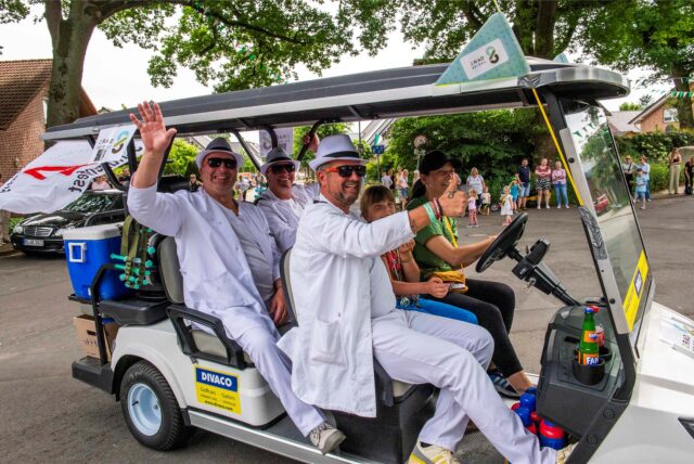 Drei Männer in weißen Anzügen in einer Art Golfwagen