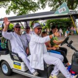Drei Männer in weißen Anzügen in einer Art Golfwagen
