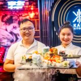 Chef Tri Dung Nguyen und eine Mitarbeiterin halten Sushi-Platten im Restaurant Kami Kitchen am Dortmunder Ostenhellweg in die Kamera