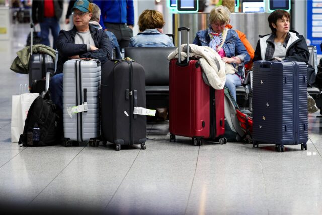 Im Abflugterminal am Flughafen Düsseldorf warten Reisende auf einer Bank sitzend mit ihren Koffern auf ihren Flug.