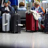 Im Abflugterminal am Flughafen Düsseldorf warten Reisende auf einer Bank sitzend mit ihren Koffern auf ihren Flug.