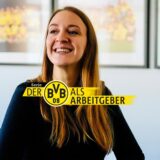 Rebecca Collmann, die die Auswärtsfahrten des BVB organisiert, vor Fotos von Erfolgen aus der Vereinsgeschichte.