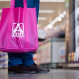 Ein Mann steht mit einer pinken Aldi-Nord-Einkaufstasche vor einem Regal in einem Aldi-Markt.