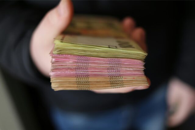 Ein Mann in schwarzem Pullover und Jeans hält einen Stapel Euro-Scheine in der Hand.
