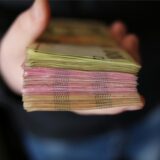 Ein Mann in schwarzem Pullover und Jeans hält einen Stapel Euro-Scheine in der Hand.