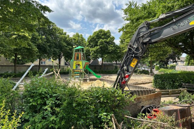 Spielplatz im Umbau mit neuem Spielturm und Bagger, alte Geräte liegen am Rand.