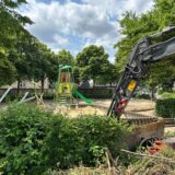 Spielplatz im Umbau mit neuem Spielturm und Bagger, alte Geräte liegen am Rand.