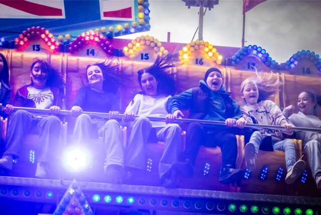 Jugendliche sitzen bei der Pfingstkirmes Huckarde auf dem Scheibenwischer-Fahrgeschäft „Jump Street“.