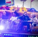 Jugendliche sitzen bei der Pfingstkirmes Huckarde auf dem Scheibenwischer-Fahrgeschäft „Jump Street“.