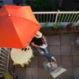 Ein Mann sitzt auf dem Balkon unter einem Sonnenschirm und liest ein Buch.