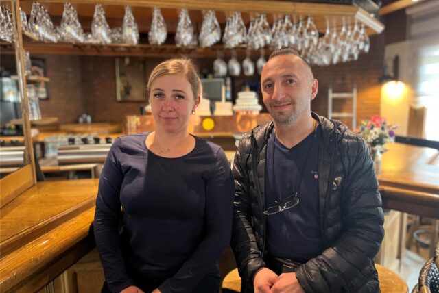 Das Bild zeigt das Restaurant „Hörder Treff“ mit seiner Außenbestuhlung. Auf der rechten Seite sind zwei Personen vor einem Tresen mit Gläsern zu sehen.