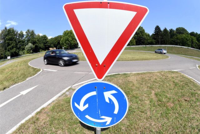 Ein Verkehrsschild weist auf einem Verkehrsübungsplatz auf einen Kreisverkehr hin.