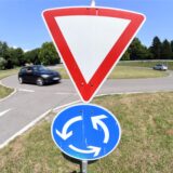Ein Verkehrsschild weist auf einem Verkehrsübungsplatz auf einen Kreisverkehr hin.