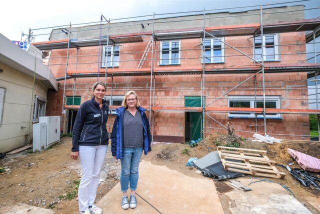 Dr. Martina Krutzinna und Silke Grobecker stehen auf einer Baustelle vor einem Anbau, der noch nicht verputzt ist.