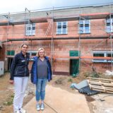 Dr. Martina Krutzinna und Silke Grobecker stehen auf einer Baustelle vor einem Anbau, der noch nicht verputzt ist.