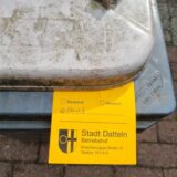 Ein gelber Zettel des Betriebshofes steckt unter dem Deckel einer Biotonne.