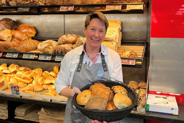Eine Verkäuferin hält einen Korb voller Brötchen.