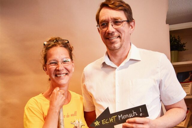 Christina und ein Mann halten ein Schild mit #ECHT Mensch