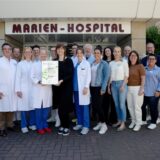 Menschen stehen vor dem Marien-Hospital Marl und halten die Zertifizierung in die Kamera.