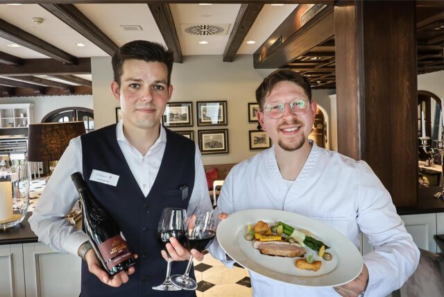 Koch Konstantin Kolombet präsentiert sein Five-Chefs-Menü im Restaurant Widu im Hotel Wittekindshof in Dortmund, während ein Kellner eine Flasche und zwei Gläser Wein hält.