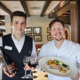 Koch Konstantin Kolombet präsentiert sein Five-Chefs-Menü im Restaurant Widu im Hotel Wittekindshof in Dortmund, während ein Kellner eine Flasche und zwei Gläser Wein hält.