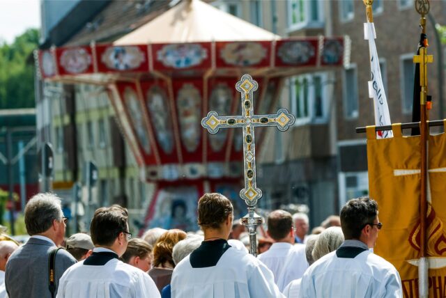 Ministranten mit Tragekreuz vor einem Kettenkarussell.