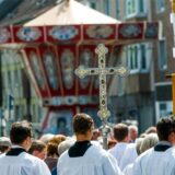 Ministranten mit Tragekreuz vor einem Kettenkarussell.
