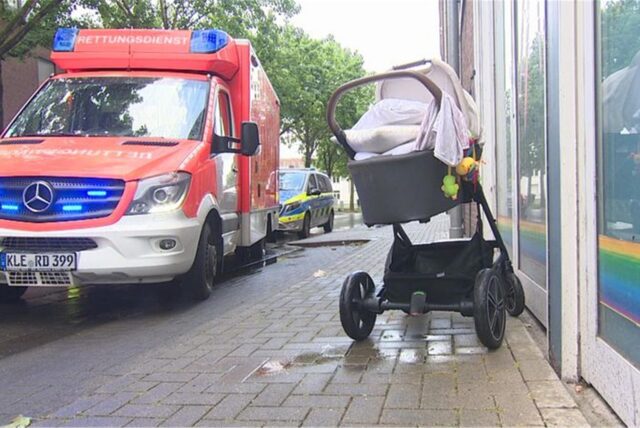 Ein durchnässter Kinderwagen steht neben einem Rettungswagen auf einem Bürgersteig.