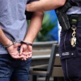 Ein Mann steht in Handschellen neben einem Polizisten (Symbolbild)