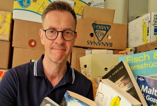 Michael Kramer mit Büchern in der Hand vor Kartons voller Büchern.