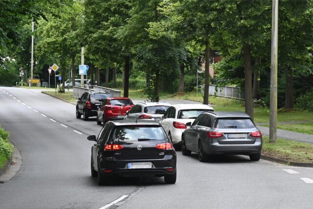 Autos parken auf der Straße, ein Auto weicht in den Gegenverkehr aus.