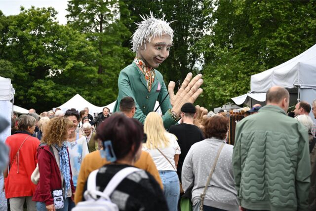 Tag zwei des Kunstmarktes 2025: Eine große Figur wird von einem Mann durch den Hertener Schlosspark getragen.