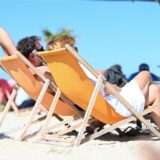 Zwei Menschen sonnen sich in Liegestühlen an einem Sandstrand
