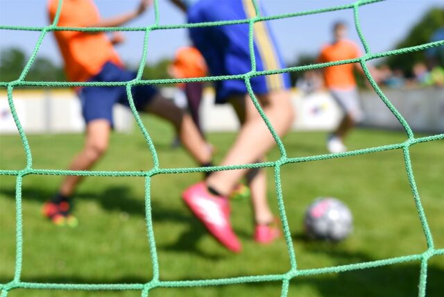 Durch ein Tornetz kann man Kinder Fußball spielen sehen.
