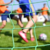 Durch ein Tornetz kann man Kinder Fußball spielen sehen.