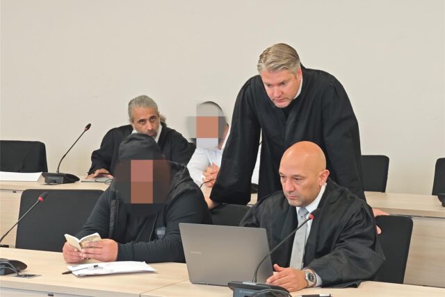 Einer der angeklagten Polizisten (hinten) und ein Mitangeklagter neben ihren Verteidigern im Essener Landgericht.