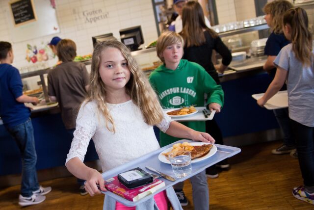 Ein Mädchen trägt ein Tablett mit Essen von einer Mensa ihrer Schule vor sich her.