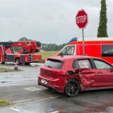 Ein beschädigtes rotes Auto steht auf einer Kreuzung. Dahinter stehen ein Rettungs- und ein Feuerwehrfahrzeug.