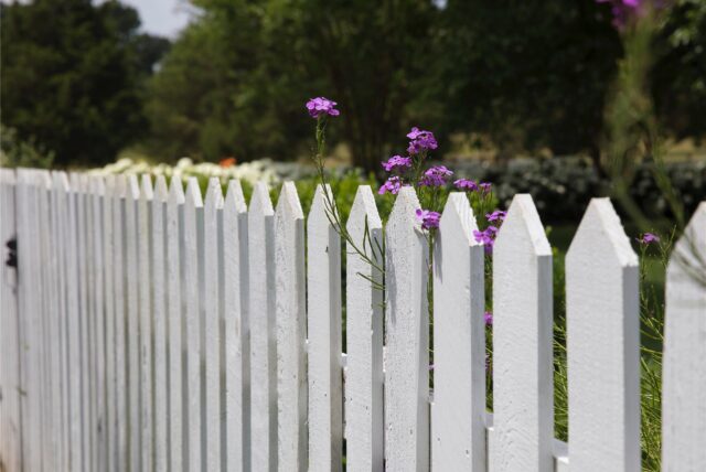 Ein weißer Gartenzaun, dahinter Blumen und Bäume