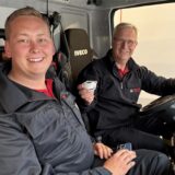 Zwei Feuerwehrleute präsentieren einen Rauchmelder im Einsatzfahrzeug