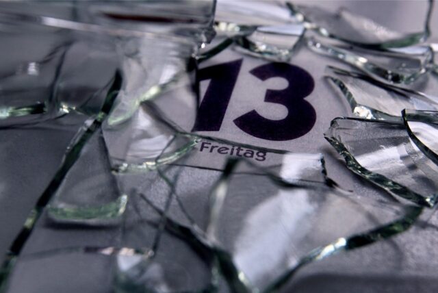 Ein Kalender zeigt Freitag, den 13. – auf dem Kalender liegen Scherben eines zerbrochenen Glases.