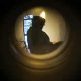 Durch das Guckloch einer Wohnungstür ist eine Person zu erkennen.