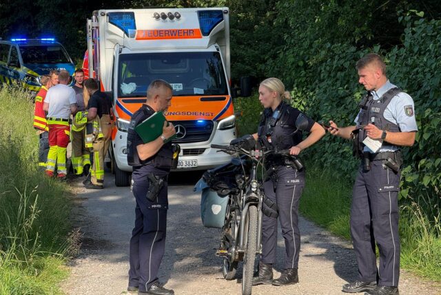 Polizisten mit einem Pedelec, im Hintergrund ein Rettungswagen